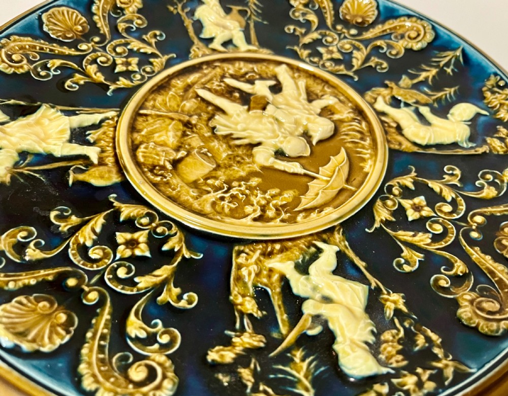 A circular Victorian majolica charger featuring relief figures of children and scrollwork in cobalt blue, ochre, and ivory glazes. View VII
