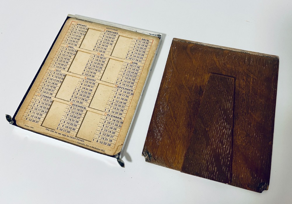 A rectangular silver frame with an engraved monogram at the top left corner housing a printed perpetual calendar card. View X