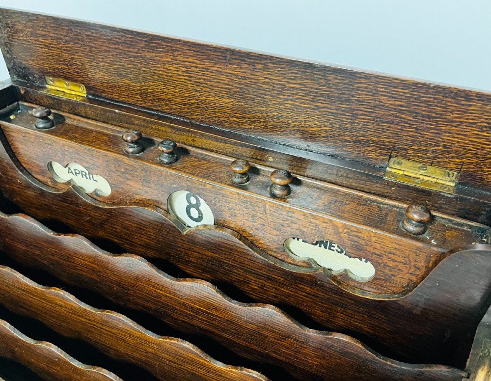 An open Victorian dark oak stationery cabinet featuring fitted letter slots, an integrated perpetual calendar, twin inkwells, and hinged side doors. View II