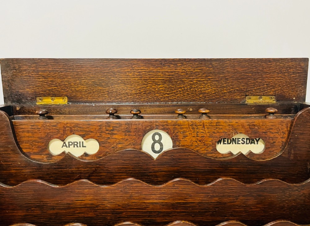 An open Victorian dark oak stationery cabinet featuring fitted letter slots, an integrated perpetual calendar, twin inkwells, and hinged side doors. View III