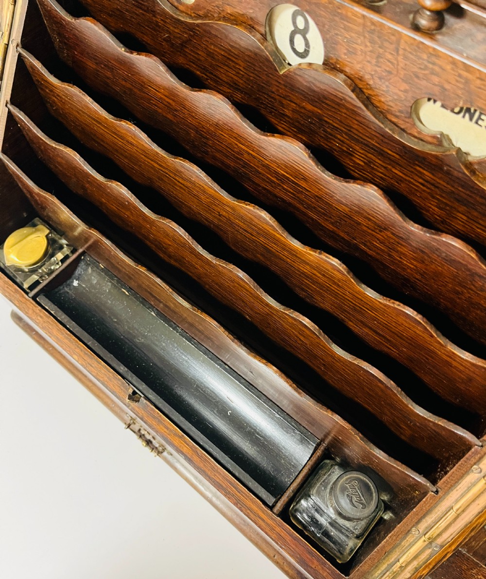 An open Victorian dark oak stationery cabinet featuring fitted letter slots, an integrated perpetual calendar, twin inkwells, and hinged side doors. View IV