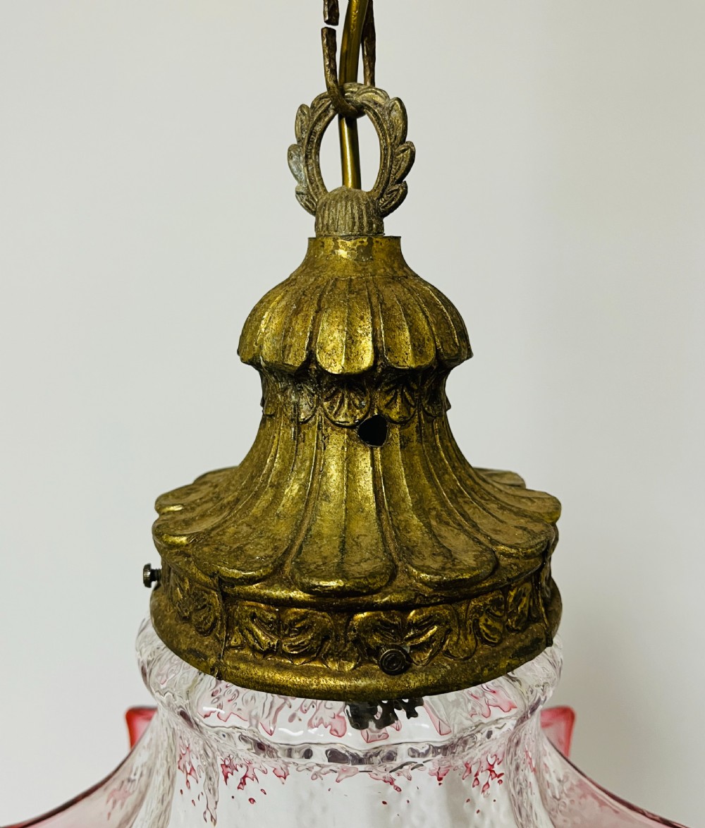 A fluted cranberry glass pendant light shade with a clear textured body and red flared rim, fitted with an ornate brass cap. View II