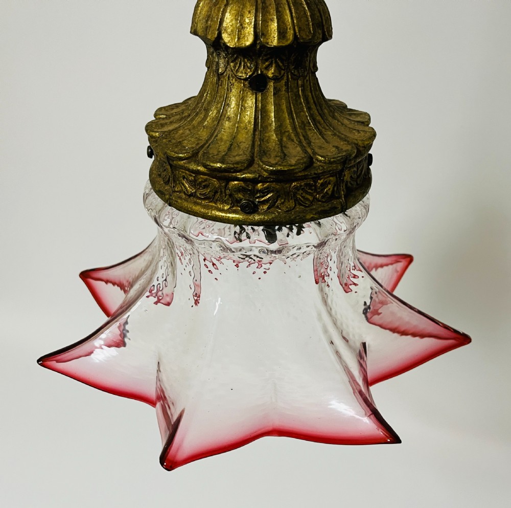A fluted cranberry glass pendant light shade with a clear textured body and red flared rim, fitted with an ornate brass cap. View III