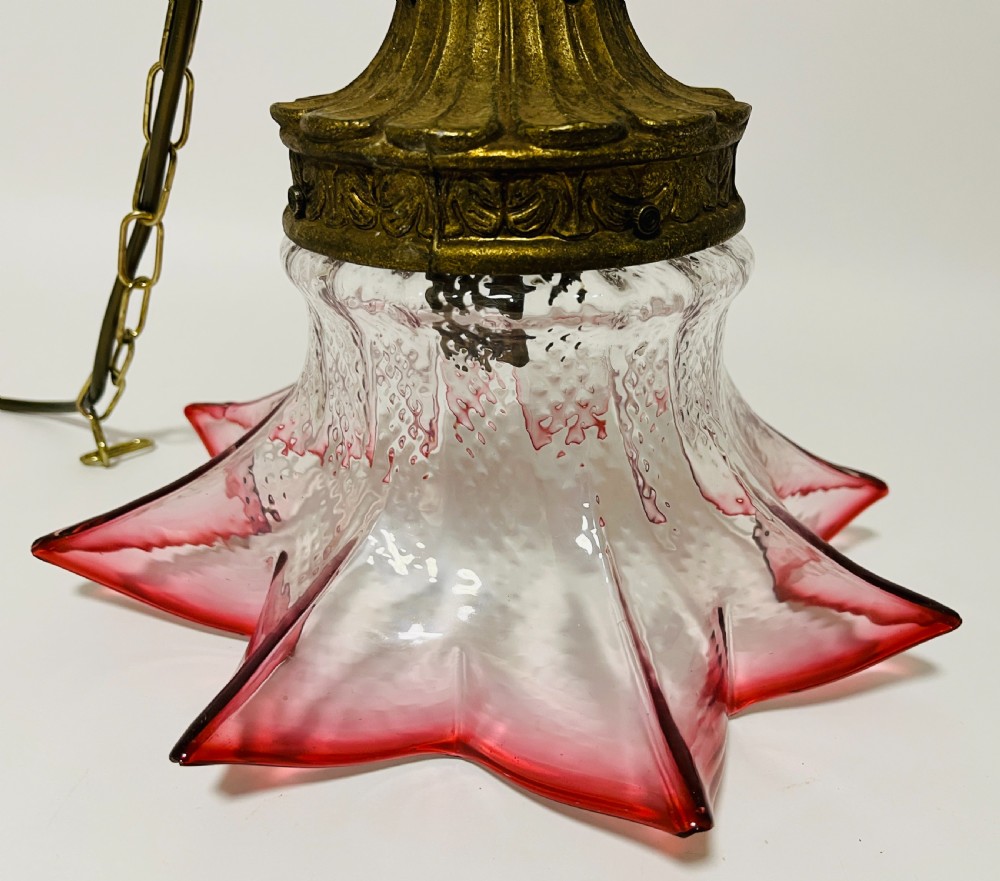 A fluted cranberry glass pendant light shade with a clear textured body and red flared rim, fitted with an ornate brass cap. View IV