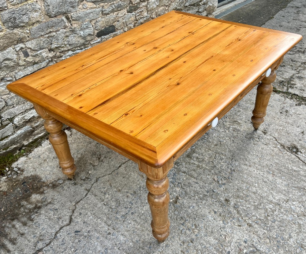 A large Victorian pine farmhouse table featuring a planked top, two frieze drawers with white ceramic knobs, and turned legs fitted with brass castors. View IV