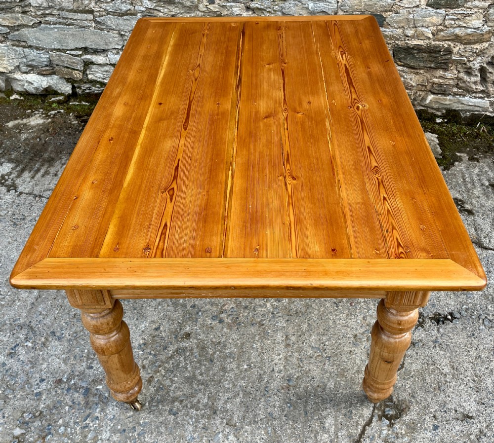 A large Victorian pine farmhouse table featuring a planked top, two frieze drawers with white ceramic knobs, and turned legs fitted with brass castors. View XII