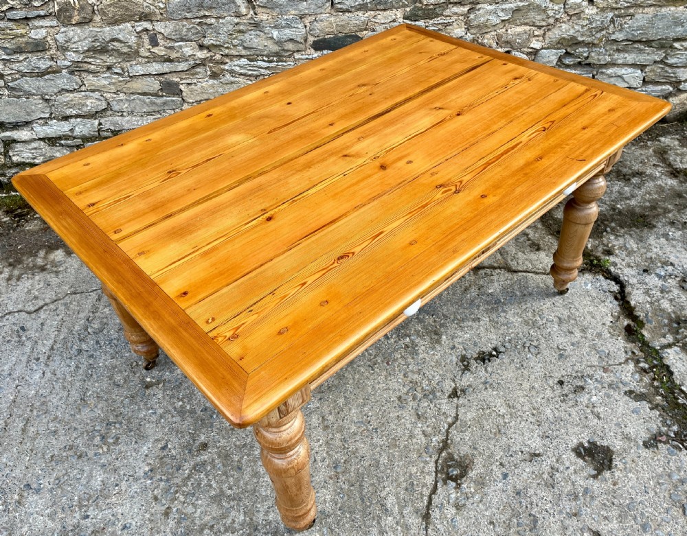 A large Victorian pine farmhouse table featuring a planked top, two frieze drawers with white ceramic knobs, and turned legs fitted with brass castors. View XIV