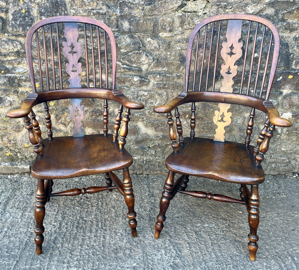 A pair of antique wooden Windsor armchairs featuring curved hoop backs, pierced central splats, broad armrests, and turned legs.