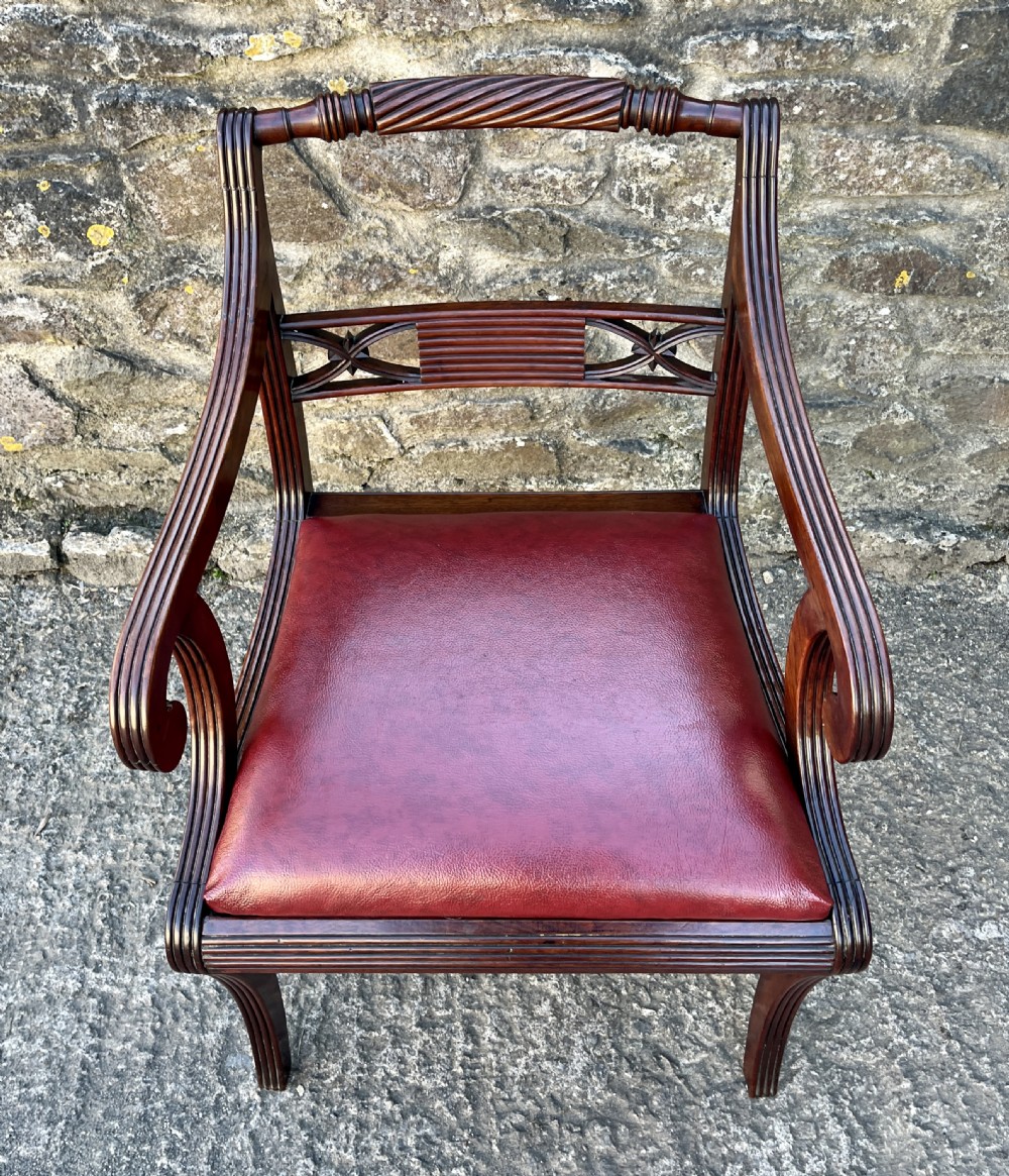A Regency mahogany armchair featuring reeded scroll arms, a carved back splat, swept legs, and a deep red leather seat. View II