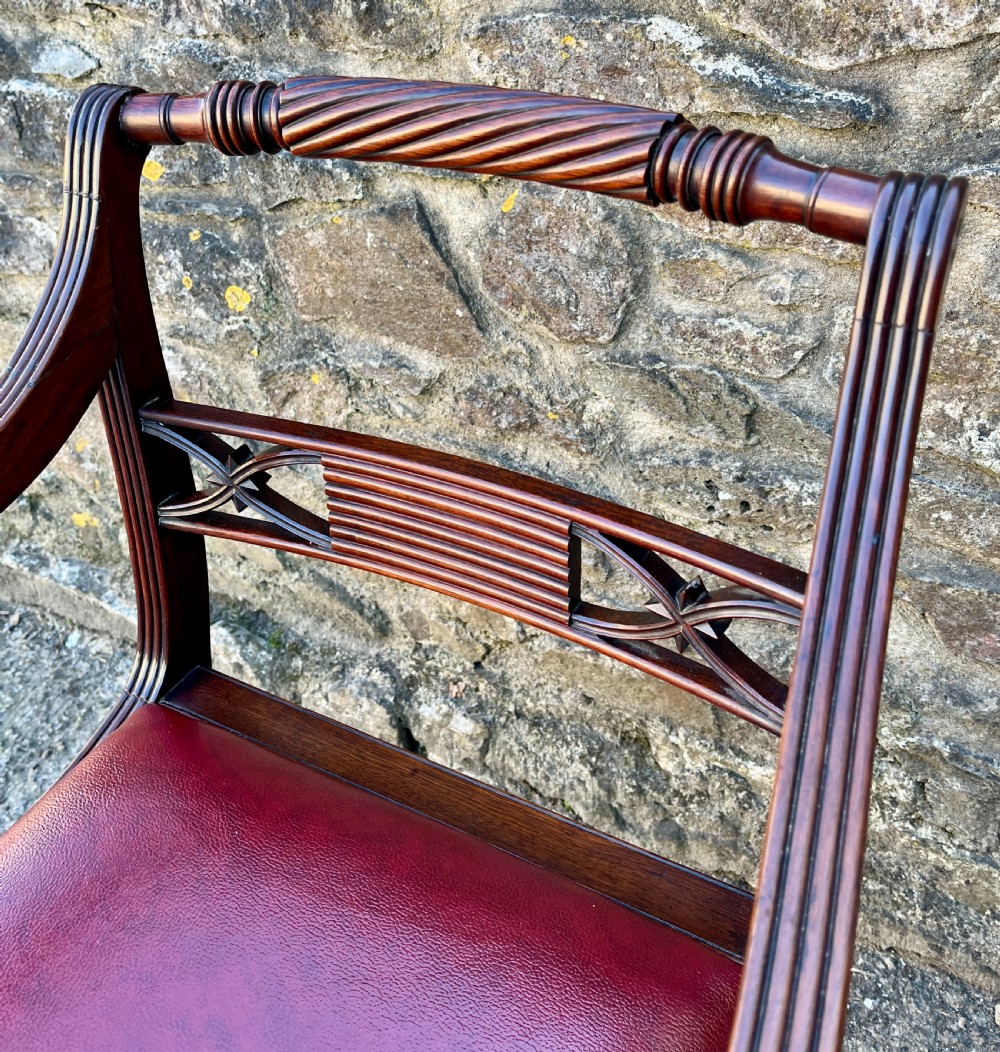 A Regency mahogany armchair featuring reeded scroll arms, a carved back splat, swept legs, and a deep red leather seat. View III