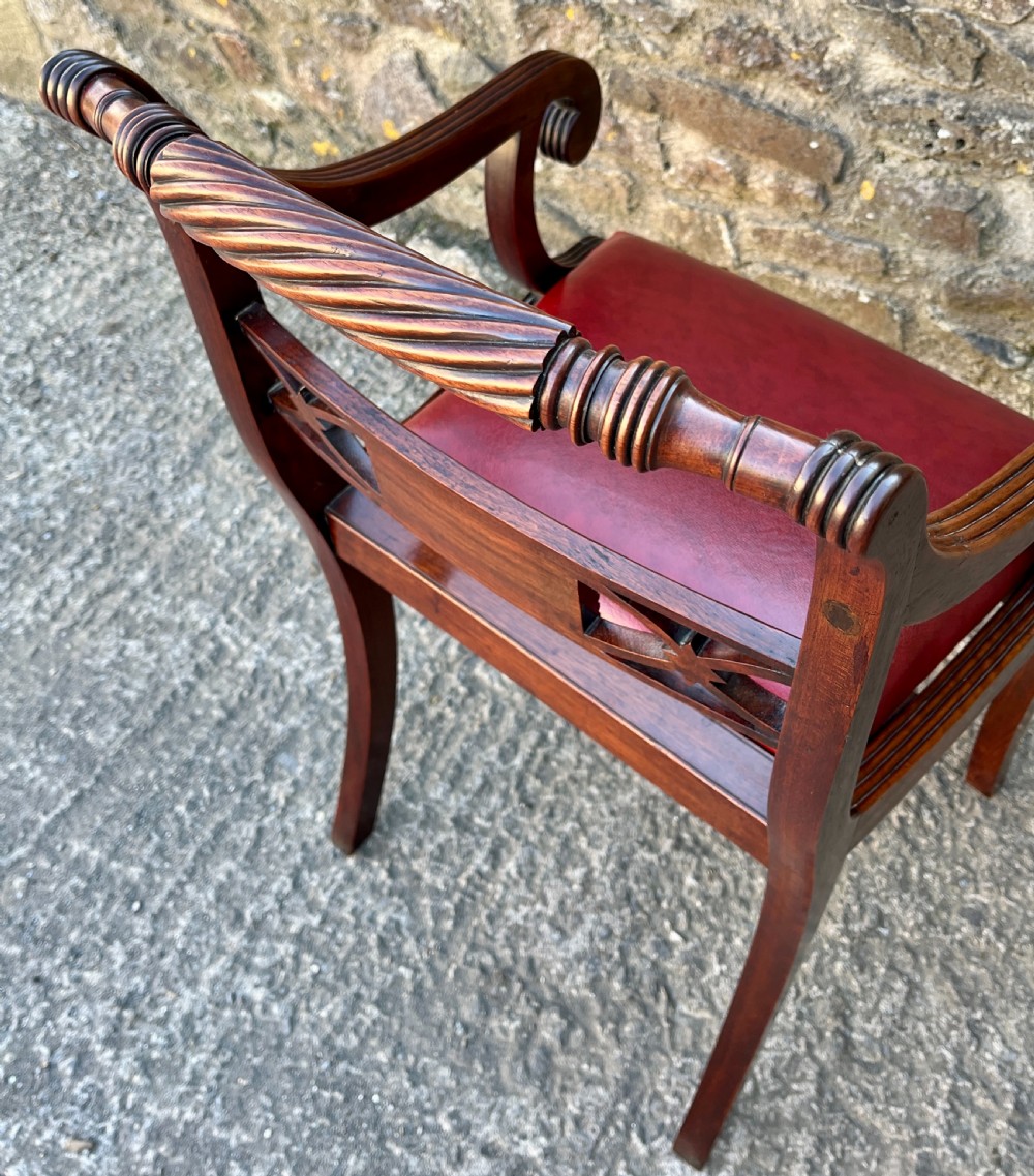 A Regency mahogany armchair featuring reeded scroll arms, a carved back splat, swept legs, and a deep red leather seat. View V