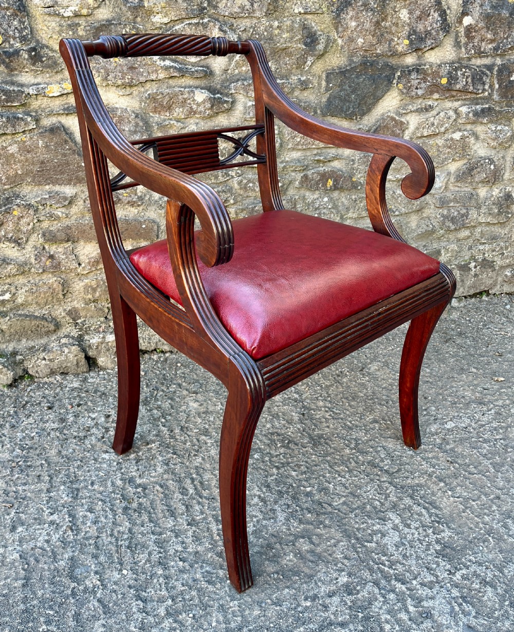 A Regency mahogany armchair featuring reeded scroll arms, a carved back splat, swept legs, and a deep red leather seat. View VI