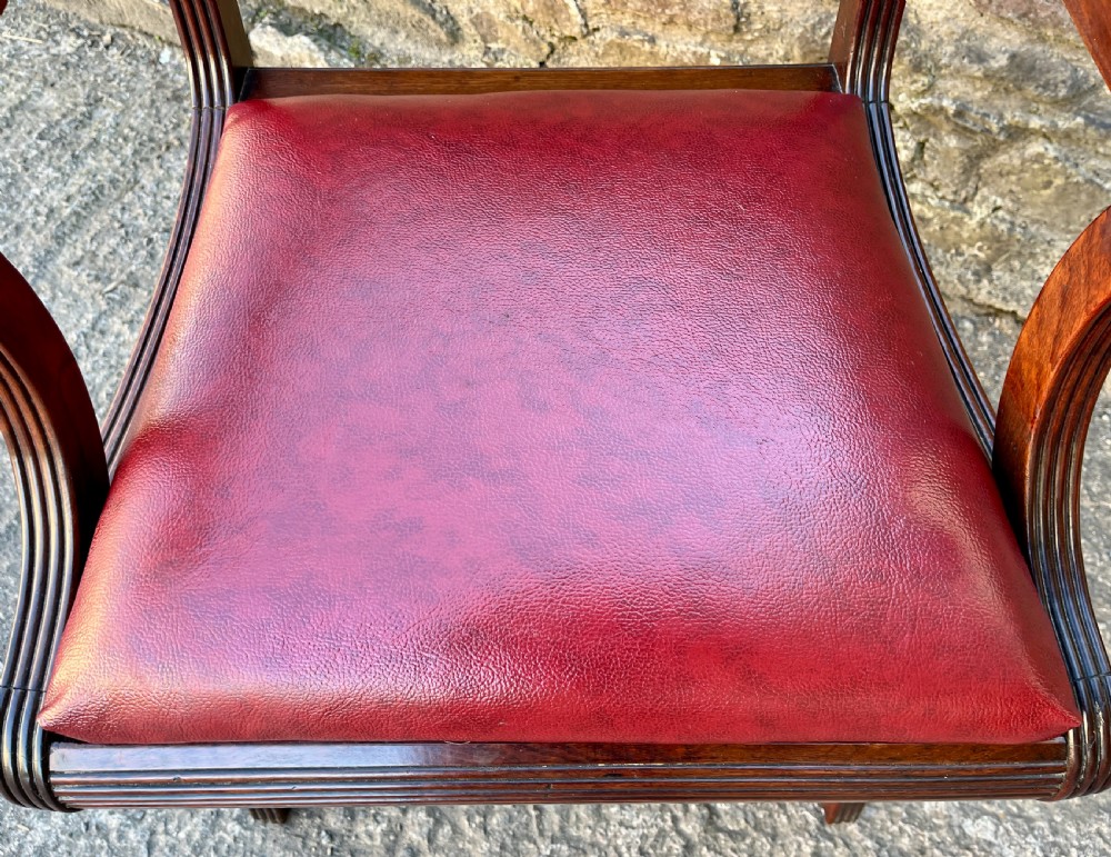 A Regency mahogany armchair featuring reeded scroll arms, a carved back splat, swept legs, and a deep red leather seat. View VII
