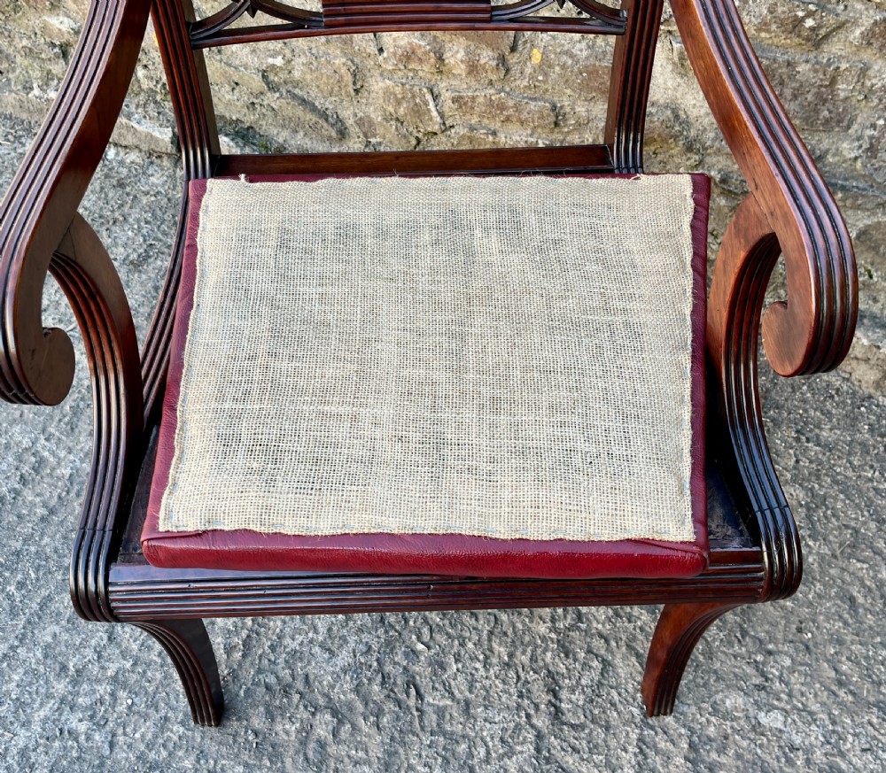 A Regency mahogany armchair featuring reeded scroll arms, a carved back splat, swept legs, and a deep red leather seat. View IX