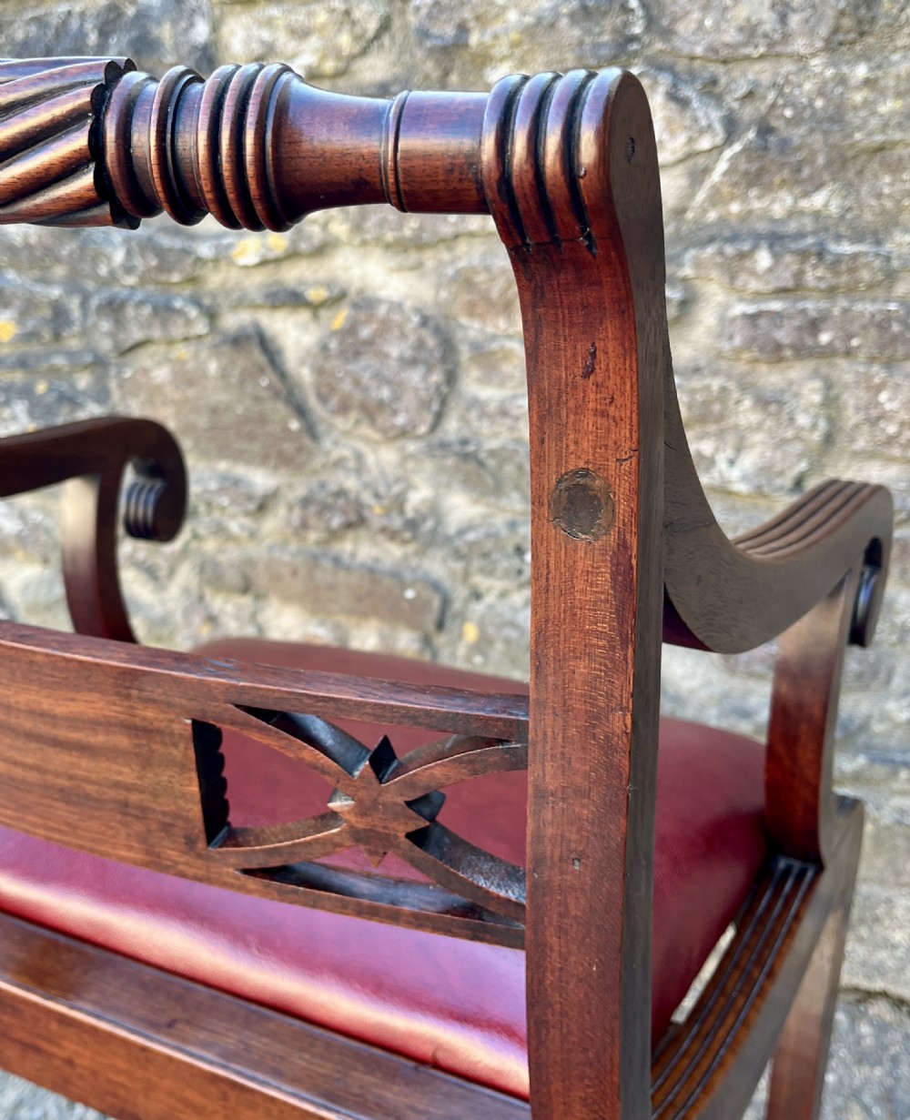A Regency mahogany armchair featuring reeded scroll arms, a carved back splat, swept legs, and a deep red leather seat. View XI