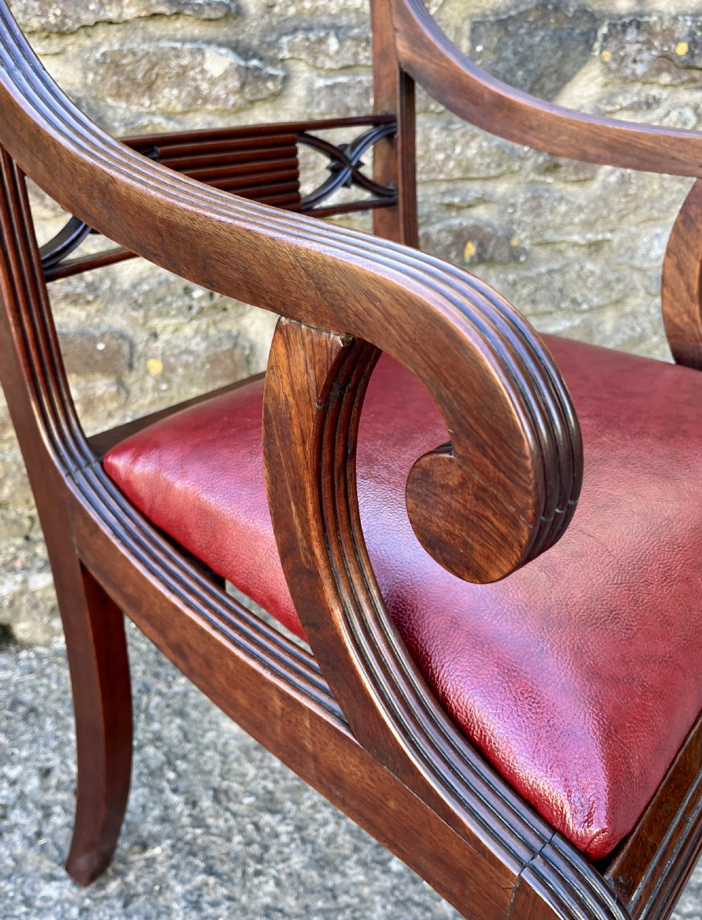 A Regency mahogany armchair featuring reeded scroll arms, a carved back splat, swept legs, and a deep red leather seat. View XII