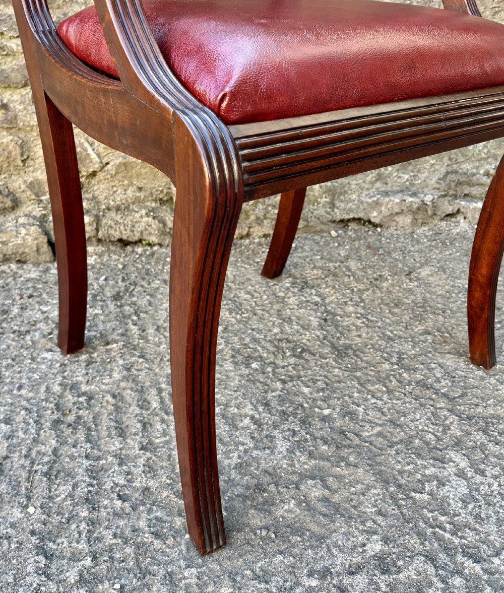 A Regency mahogany armchair featuring reeded scroll arms, a carved back splat, swept legs, and a deep red leather seat. View XIII