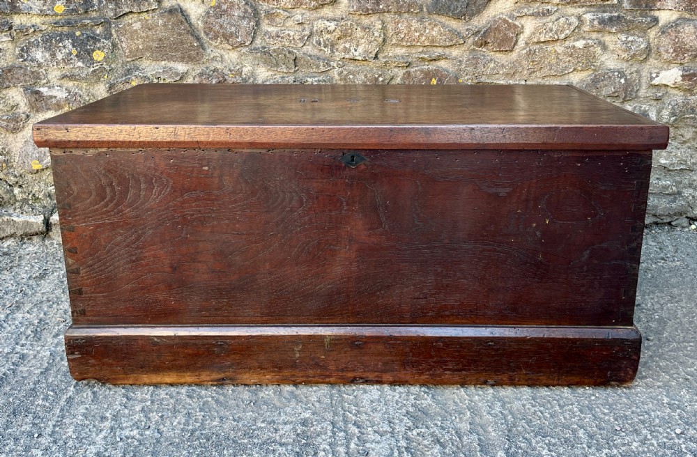 A rectangular dark teak blanket chest featuring carved initials on the hinged lid, exposed dovetail joints, and a keyhole escutcheon on the front. View II