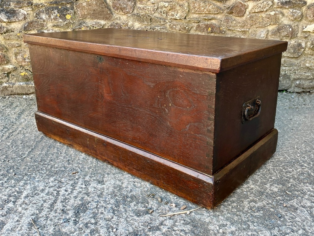 A rectangular dark teak blanket chest featuring carved initials on the hinged lid, exposed dovetail joints, and a keyhole escutcheon on the front. View VII