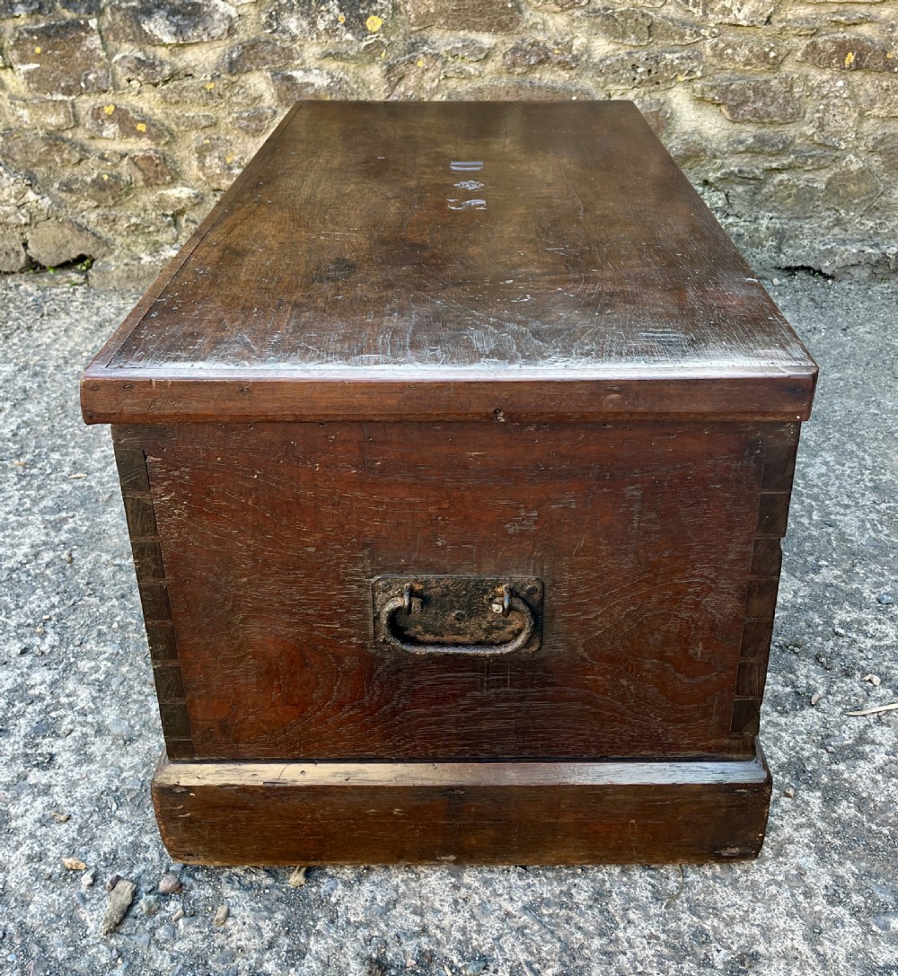A rectangular dark teak blanket chest featuring carved initials on the hinged lid, exposed dovetail joints, and a keyhole escutcheon on the front. View VIII