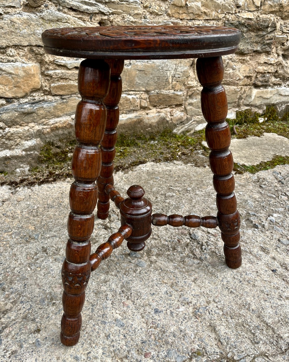 A small dark oak tripod table featuring bobbin-turned legs, a central turned stretcher, and a circular top hand-carved with floral patterns. View IV