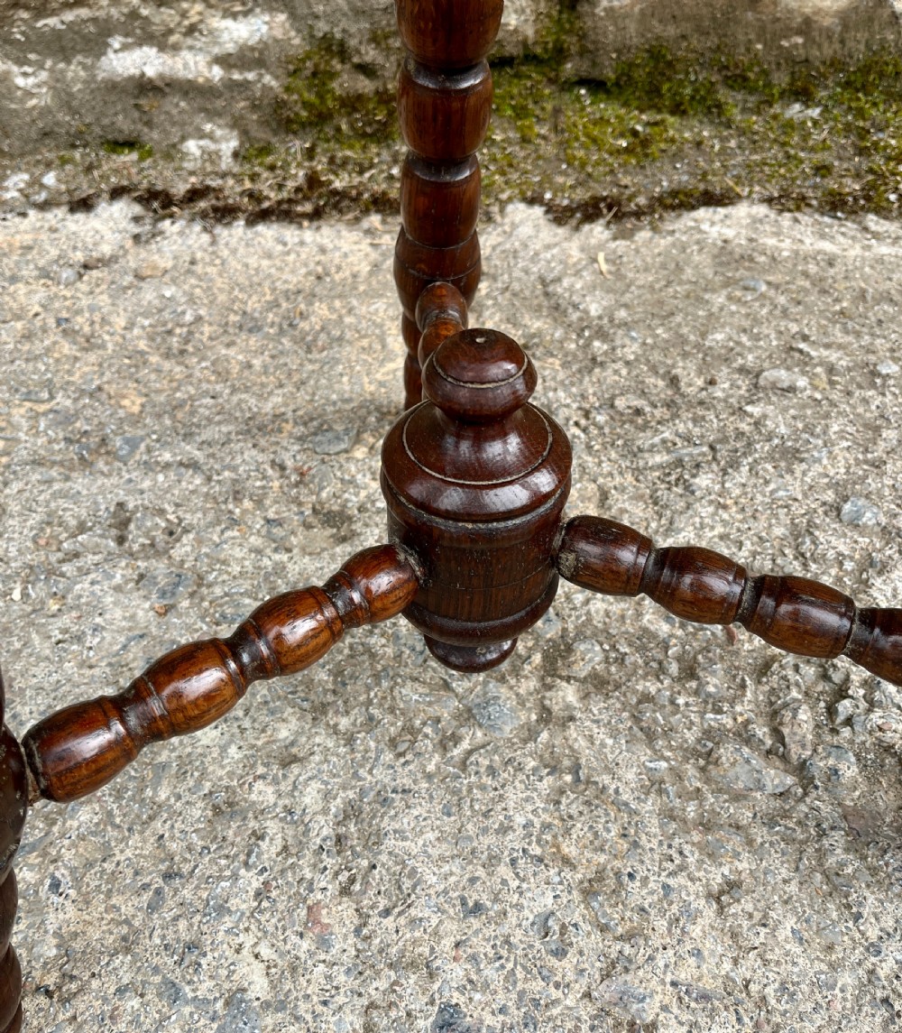 A small dark oak tripod table featuring bobbin-turned legs, a central turned stretcher, and a circular top hand-carved with floral patterns. View V