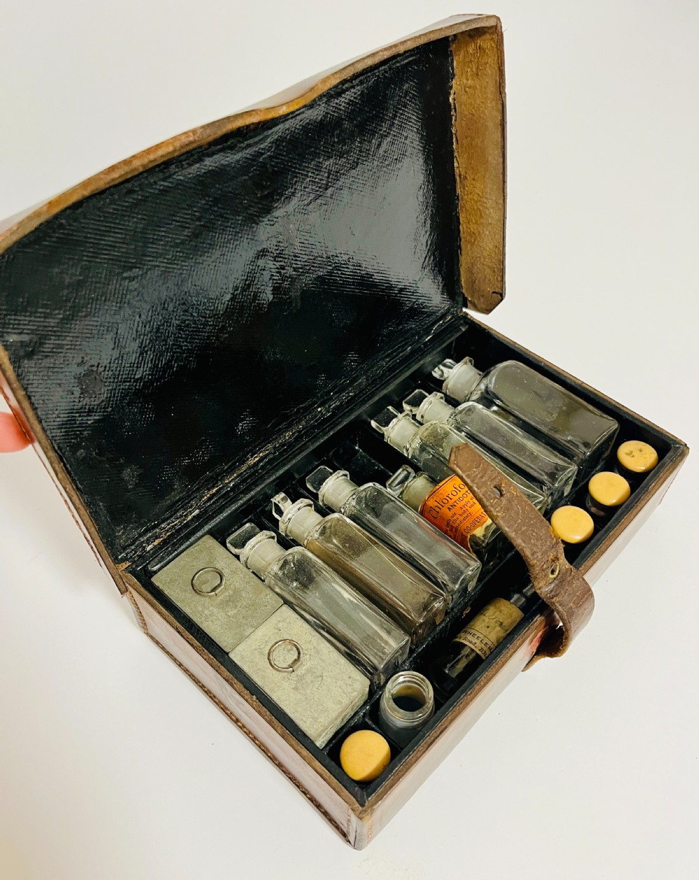 An open Victorian brown leather apothecary case revealing fitted compartments containing glass medicine bottles with stoppers and small metal tins.