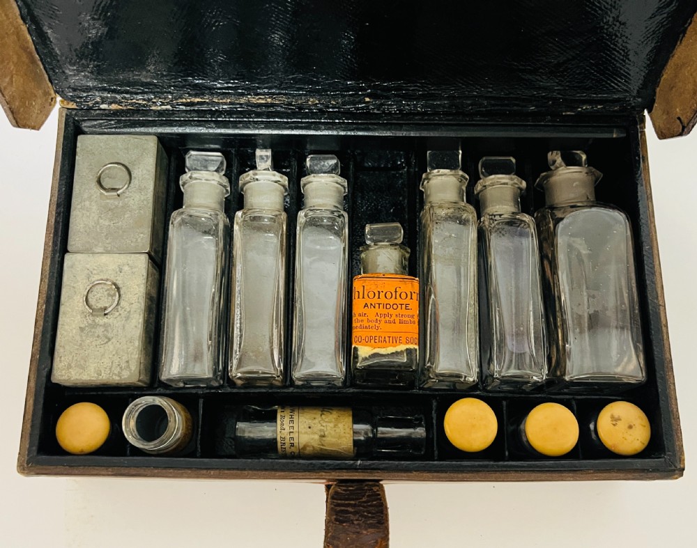 An open Victorian brown leather apothecary case revealing fitted compartments containing glass medicine bottles with stoppers and small metal tins. View II