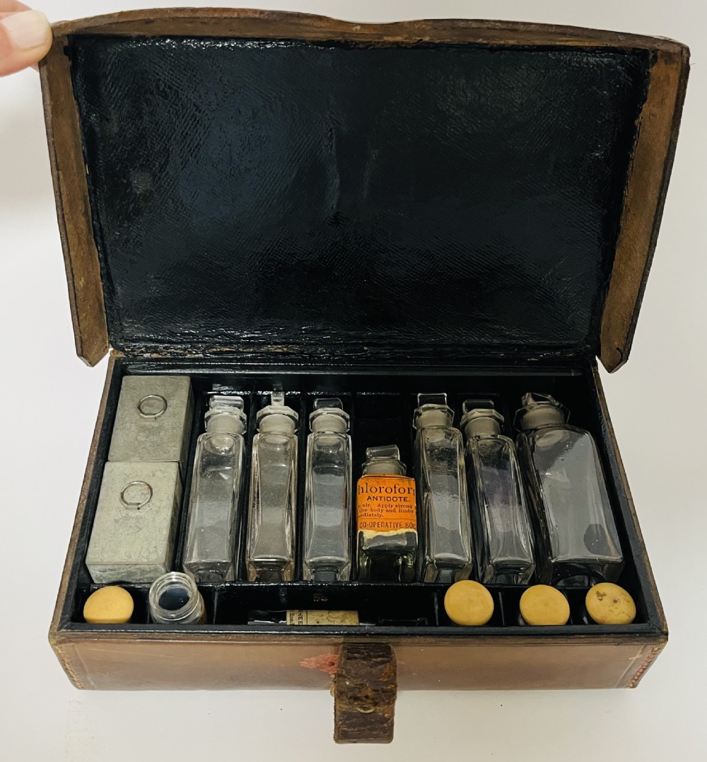An open Victorian brown leather apothecary case revealing fitted compartments containing glass medicine bottles with stoppers and small metal tins. View III