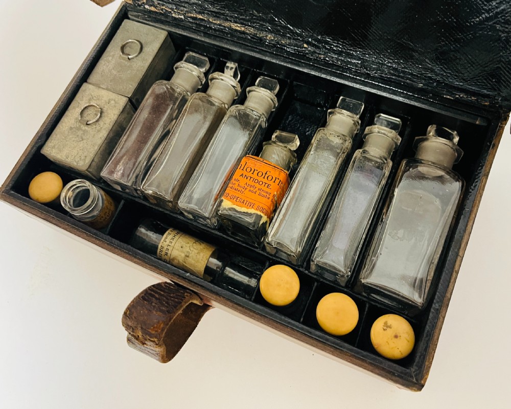 An open Victorian brown leather apothecary case revealing fitted compartments containing glass medicine bottles with stoppers and small metal tins. View IV