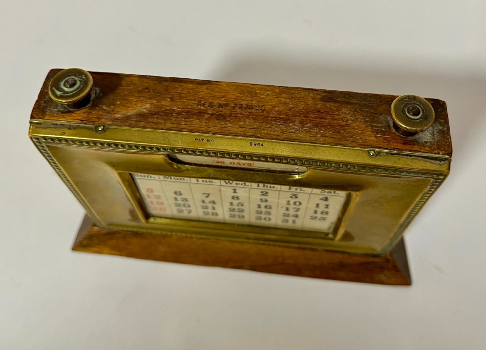An antique brass perpetual desk calendar with a beaded frame mounted on a dark oak wooden base. View VI
