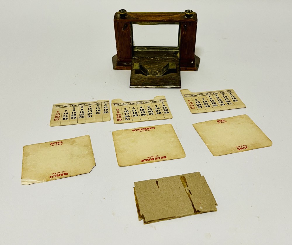 An antique brass perpetual desk calendar with a beaded frame mounted on a dark oak wooden base. View VII