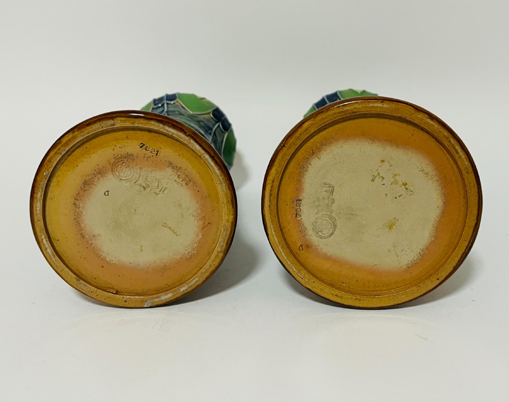 A pair of Royal Doulton Art Nouveau stoneware vases featuring mottled blue glaze, green stylised leaf rims, and ochre flared bases. View VI