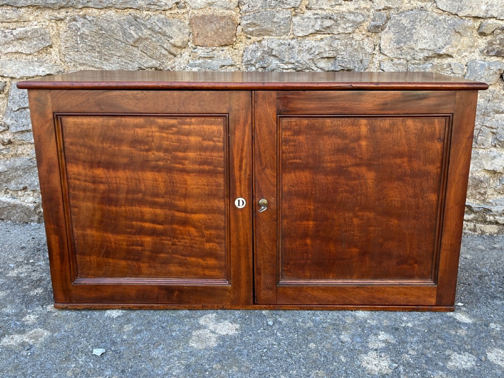 A low Victorian mahogany filing cabinet featuring twin panelled doors with flame mahogany veneer and a central keyhole.