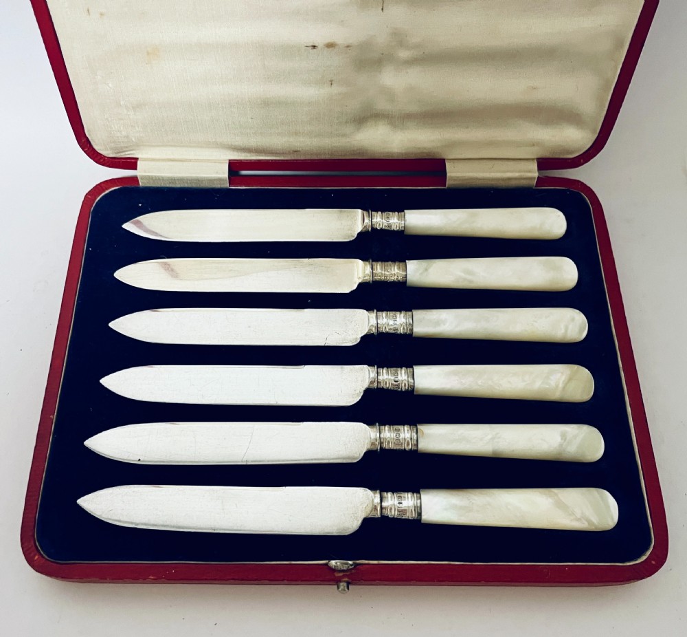 A set of six antique silver dessert knives with iridescent mother-of-pearl handles presented inside an open red velvet-lined presentation case. View II