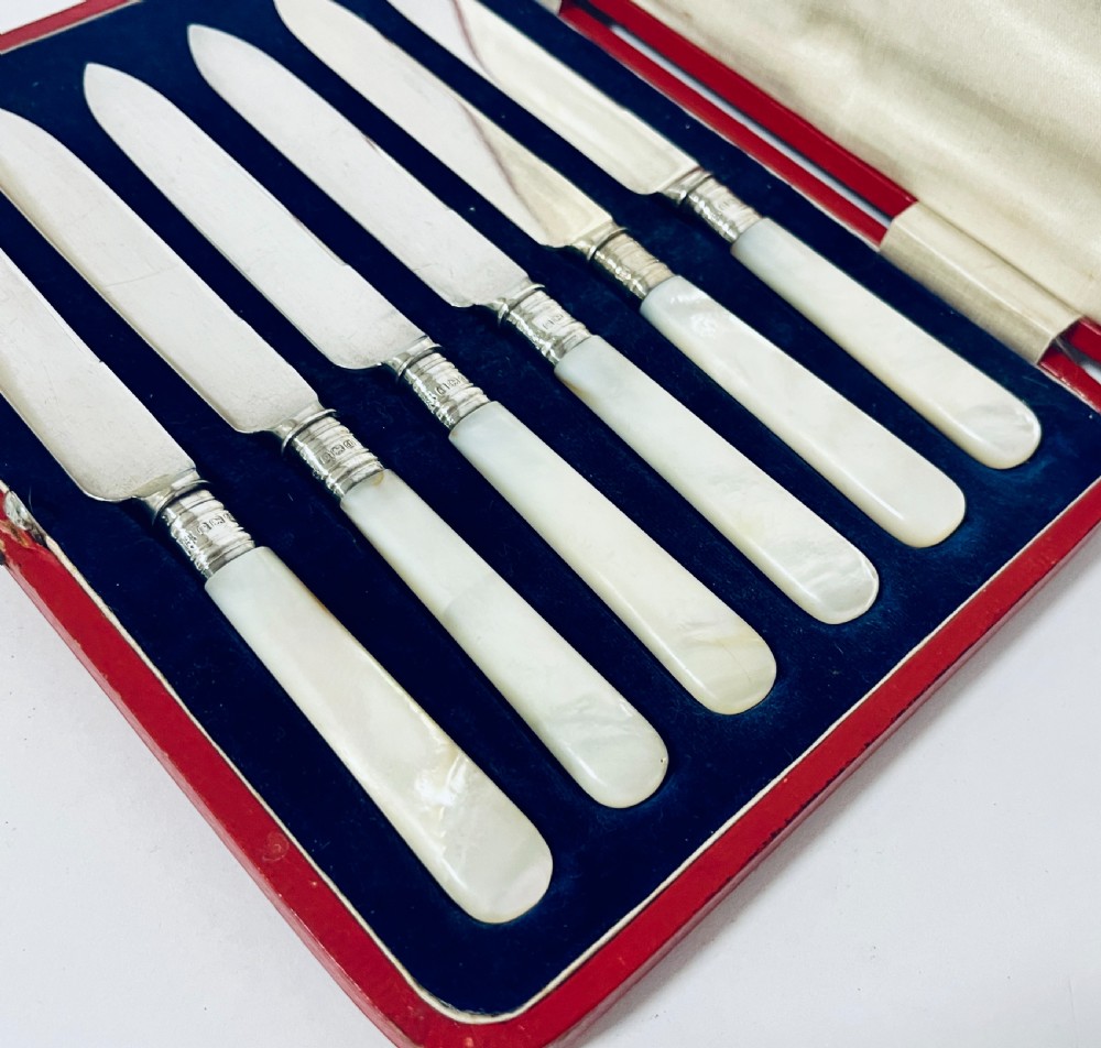 A set of six antique silver dessert knives with iridescent mother-of-pearl handles presented inside an open red velvet-lined presentation case. View III
