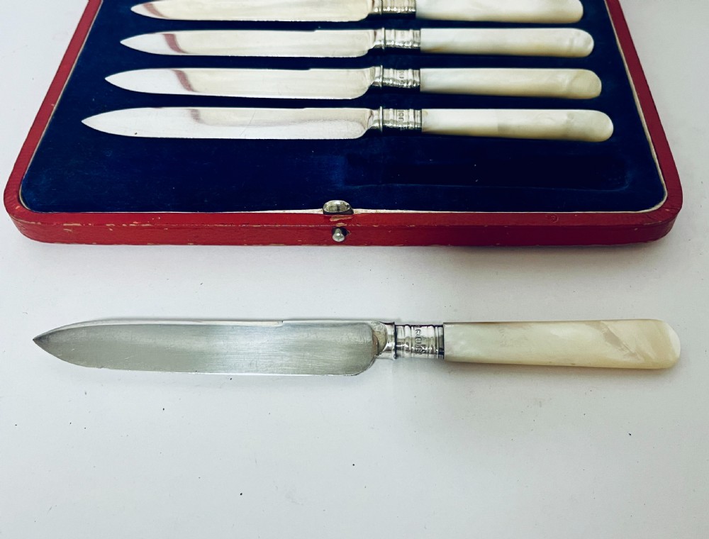 A set of six antique silver dessert knives with iridescent mother-of-pearl handles presented inside an open red velvet-lined presentation case. View VII
