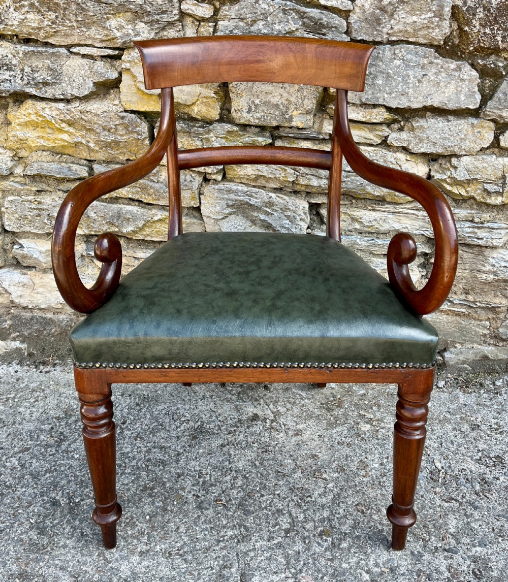Victorian mahogany carver chair featuring dramatically scrolled armrests, a curved top rail, turned front legs, and a dark green leather seat trimmed with brass studs.