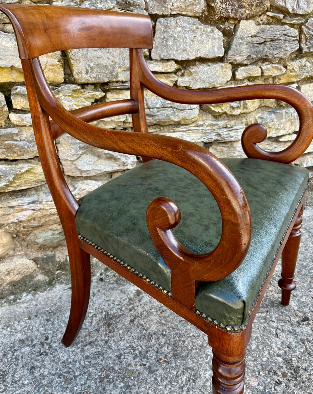 Victorian mahogany carver chair featuring dramatically scrolled armrests, a curved top rail, turned front legs, and a dark green leather seat trimmed with brass studs. View IV