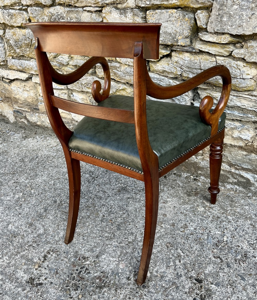 Victorian mahogany carver chair featuring dramatically scrolled armrests, a curved top rail, turned front legs, and a dark green leather seat trimmed with brass studs. View VI