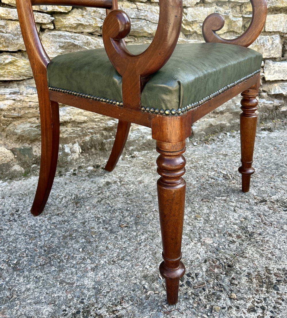 Victorian mahogany carver chair featuring dramatically scrolled armrests, a curved top rail, turned front legs, and a dark green leather seat trimmed with brass studs. View VII