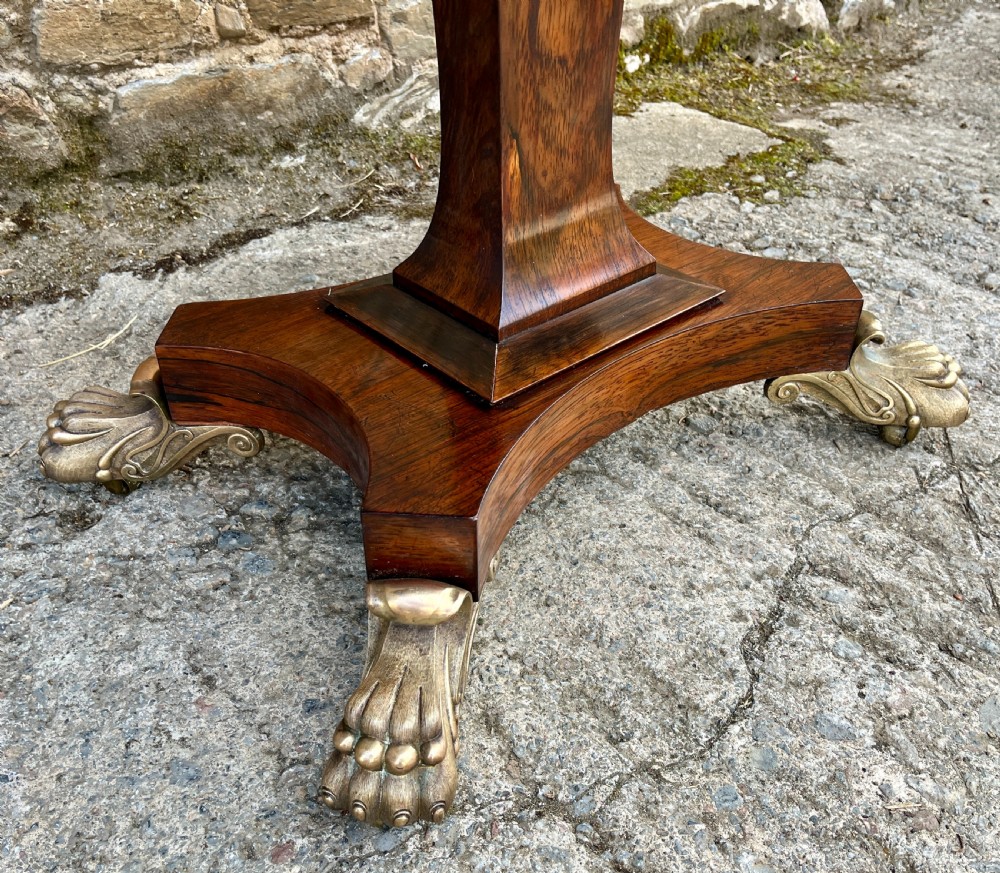 An antique Regency rosewood card table featuring a rectangular fold-over top, central tapered pedestal support, and a quadform base with brass claw feet. View IV