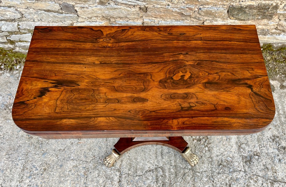 An antique Regency rosewood card table featuring a rectangular fold-over top, central tapered pedestal support, and a quadform base with brass claw feet. View VII