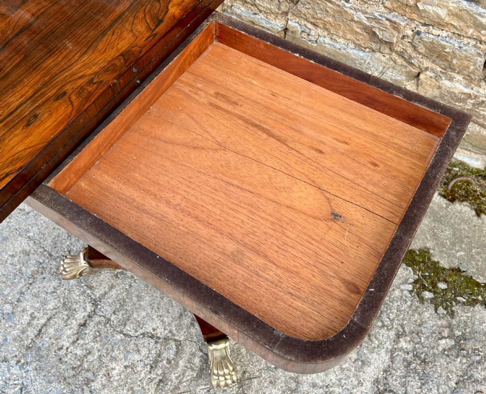 An antique Regency rosewood card table featuring a rectangular fold-over top, central tapered pedestal support, and a quadform base with brass claw feet. View IX