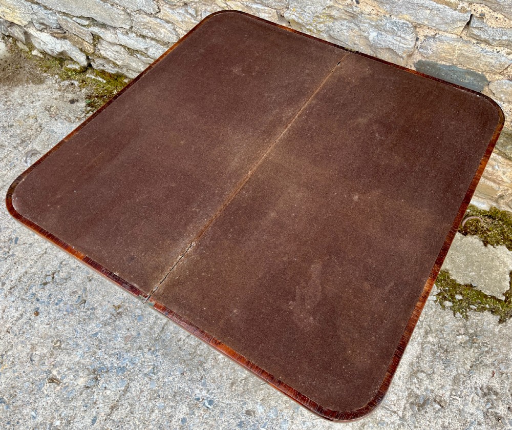 An antique Regency rosewood card table featuring a rectangular fold-over top, central tapered pedestal support, and a quadform base with brass claw feet. View XII