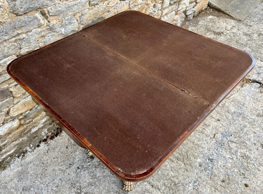 An antique Regency rosewood card table featuring a rectangular fold-over top, central tapered pedestal support, and a quadform base with brass claw feet. View XIV