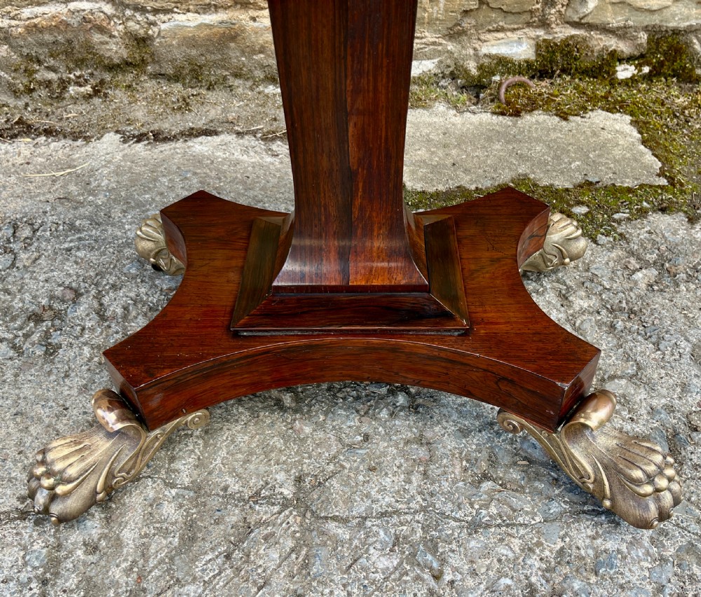 An antique Regency rosewood card table featuring a rectangular fold-over top, central tapered pedestal support, and a quadform base with brass claw feet. View XIX