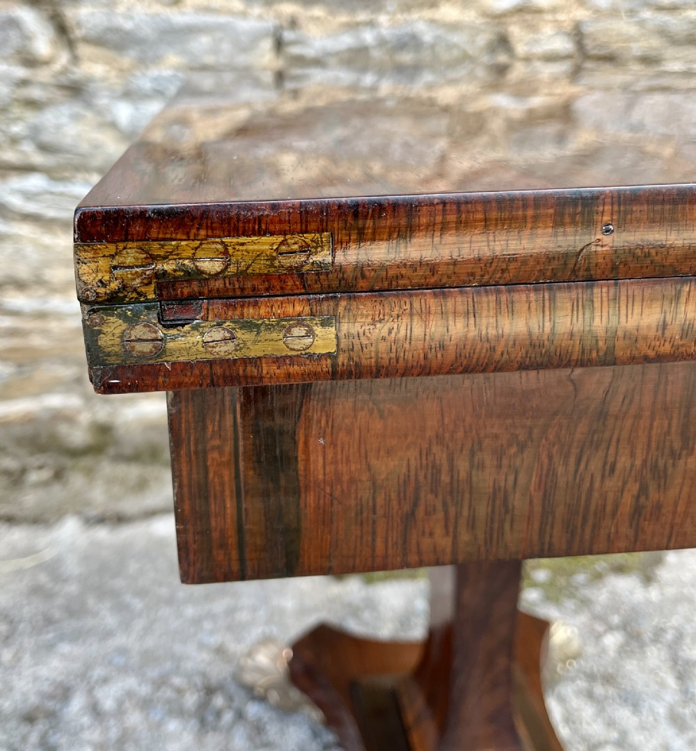 An antique Regency rosewood card table featuring a rectangular fold-over top, central tapered pedestal support, and a quadform base with brass claw feet. View XXII