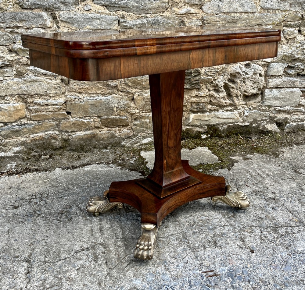 An antique Regency rosewood card table featuring a rectangular fold-over top, central tapered pedestal support, and a quadform base with brass claw feet. View XXIII