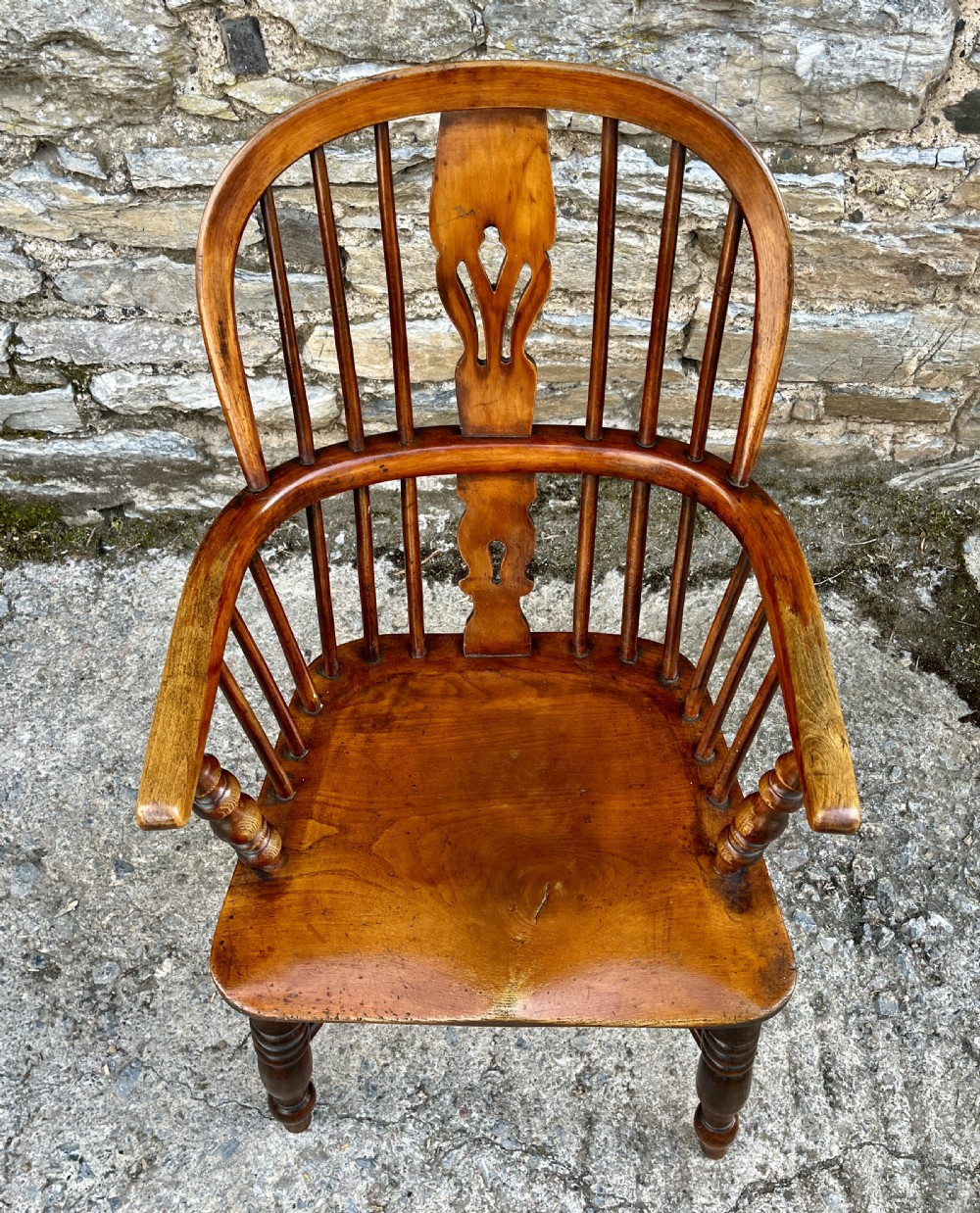 A warm brown wooden Windsor armchair featuring a curved hoop back, central pierced splat, turned spindles, shaped armrests, turned legs, and a crinoline stretcher. View III